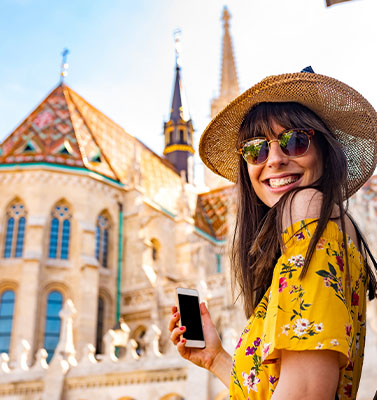 Woman with a yellow dress and hat holding a phone in an exotic locale